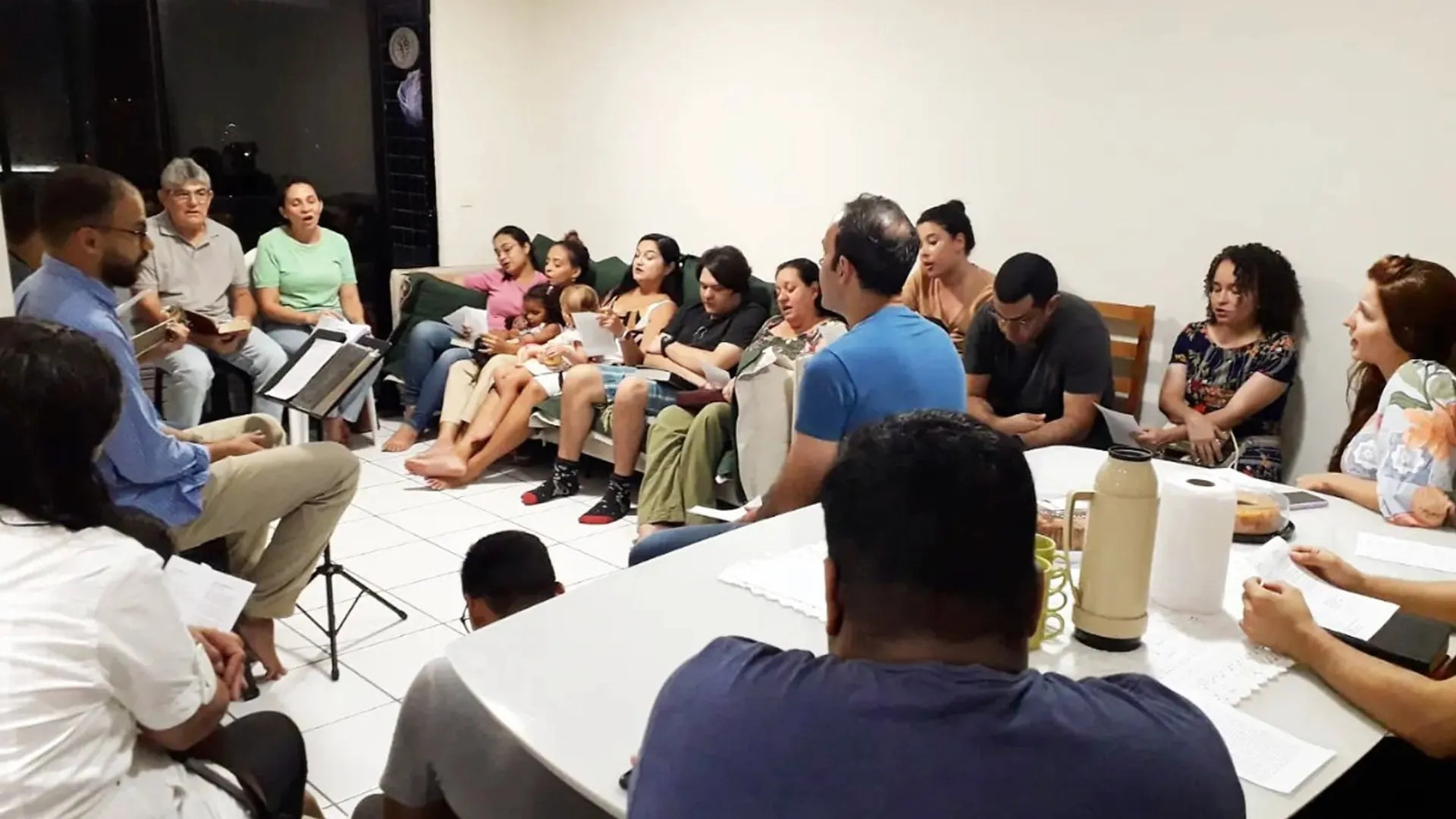 Pequeno grupo reunido em uma sala de apartamento, cantando durante o culto doméstico